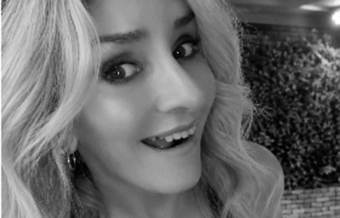 Black-and-white photograph of Stevie smiling sideways at the camera in front of a hedge wall